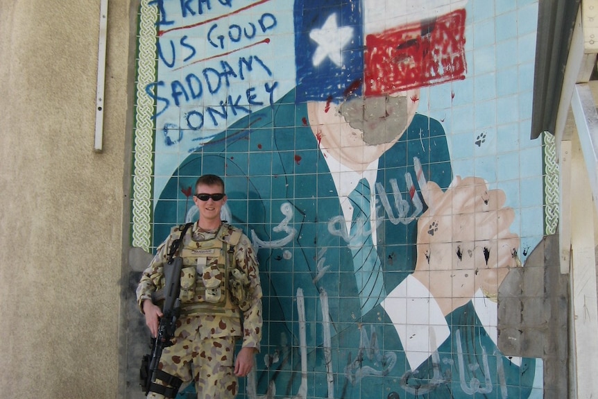 Rodney Hargrave poses with his weapon in front of a Saddam Hussein painting graffiti-ed with the words: 'US GOOD SADDAM DONKEY'