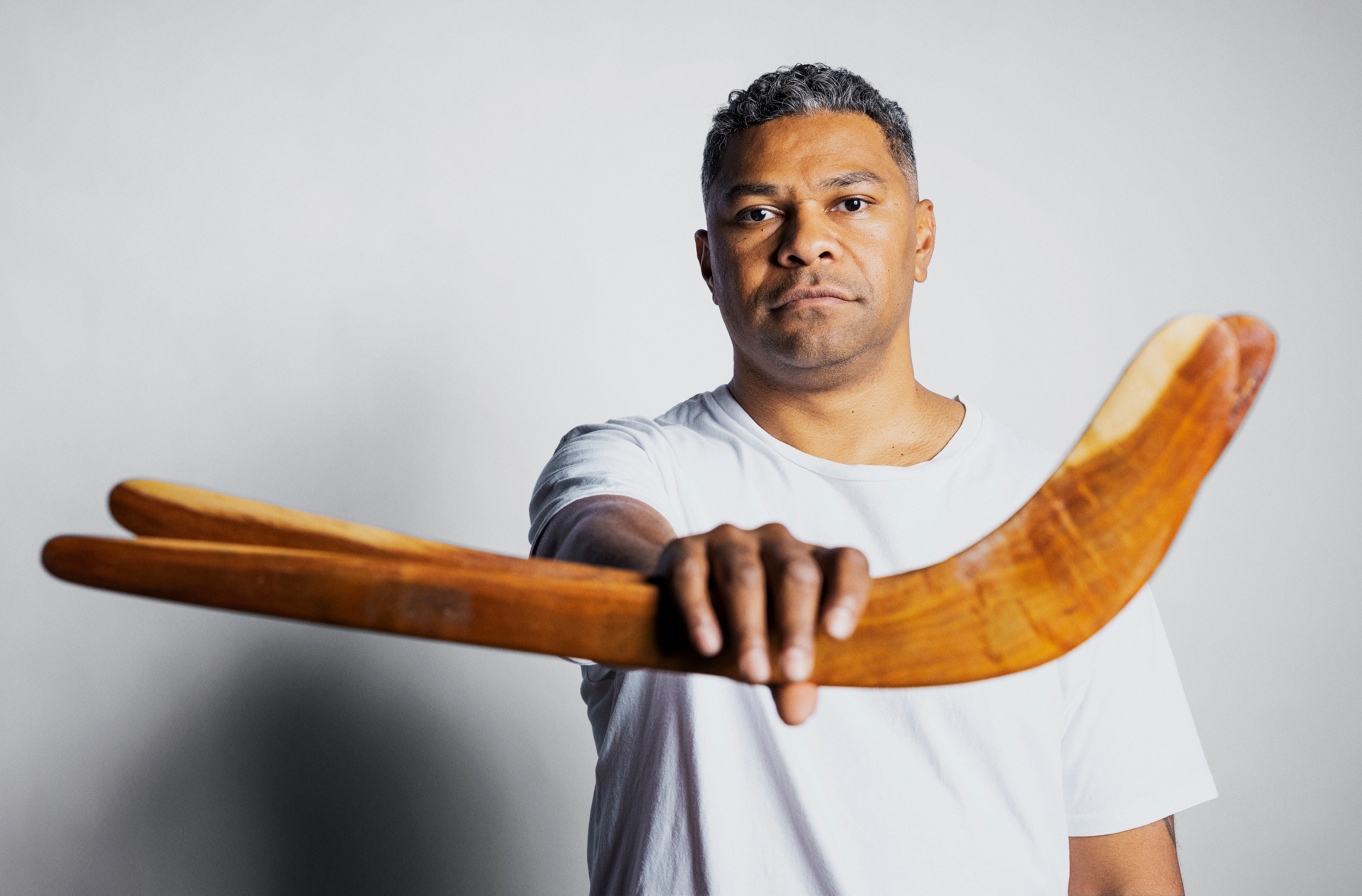 A dark-skinned man in a white T-shirt holding a boomerang stood in front of him.