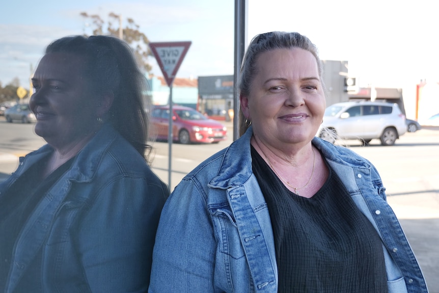 A woman in a denim jacket and a dark shirt stands against a window. Ausnew Home Care, NDIS registered provider, My Aged Care