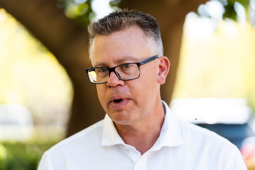 Evan Hall speaking to journalists at a park.