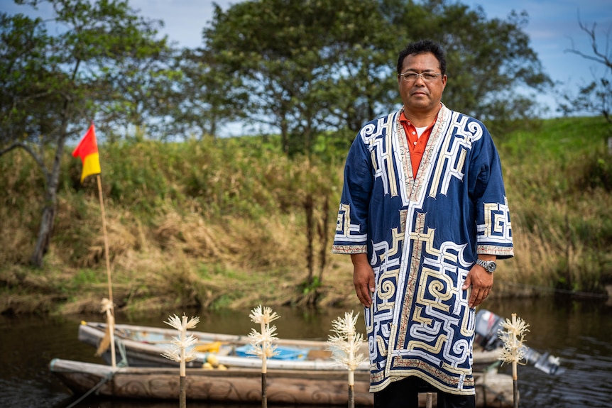 A man in a traditional robe stands at a river bank 
