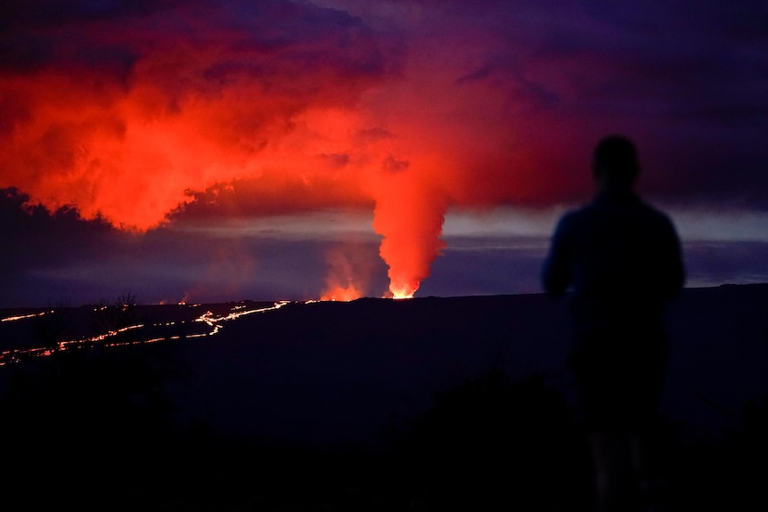 The silhouette of a person is pictured as smoke and ash are being blown into the sky by the volcano's eruption