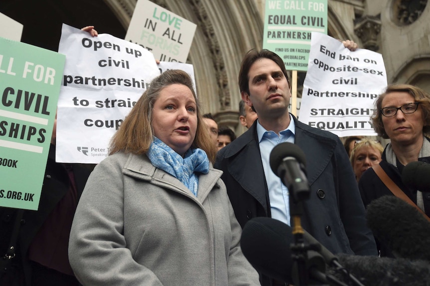 Rebecca Steinfeld and Charles Keidan speak to the media outside court with supporting protesters behind them.