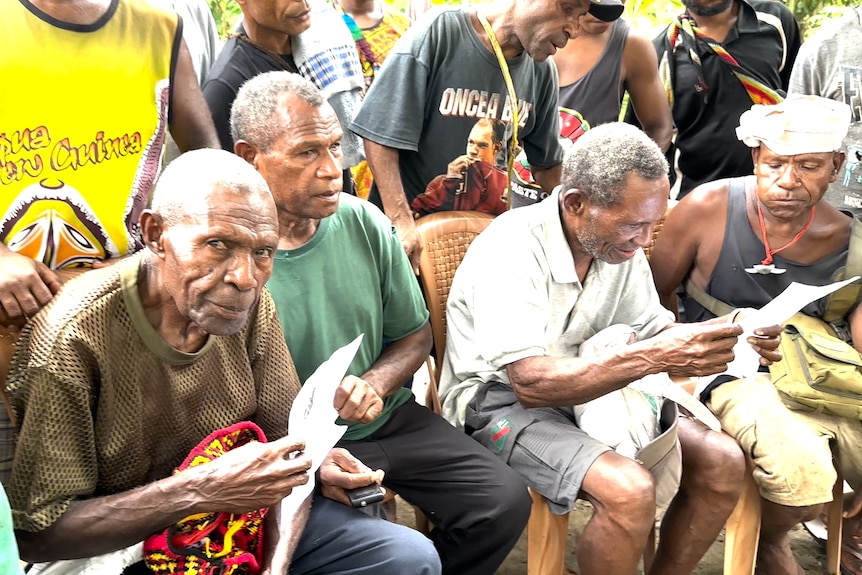 Villagers sit down and look at a catalogue of ancestors from Rai Coast whose remains are in the University of Sydney.