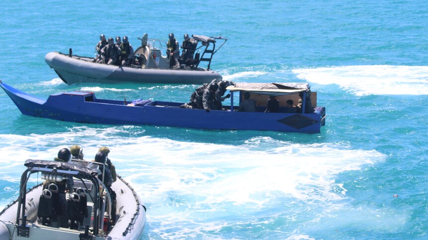 Three boats, some with military people onboard, in blue ocean