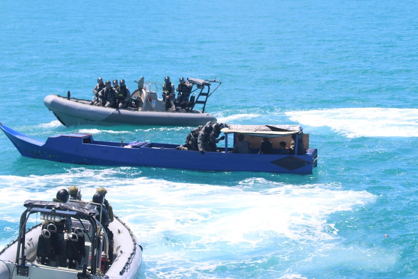 Three boats, some with military people onboard, in blue ocean