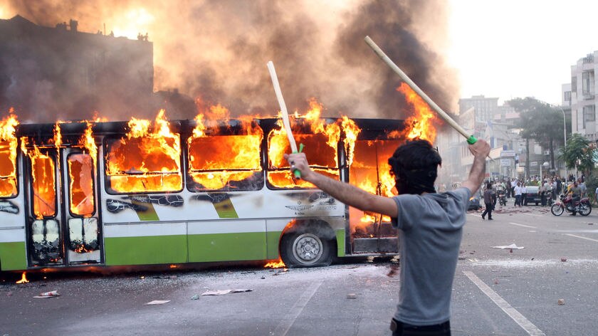 An Iranian protester stands next to a burning bus