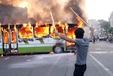 An Iranian protester stands next to a burning bus