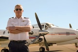 A pilot stands, arms crossed, in front of a small RFDS plane.