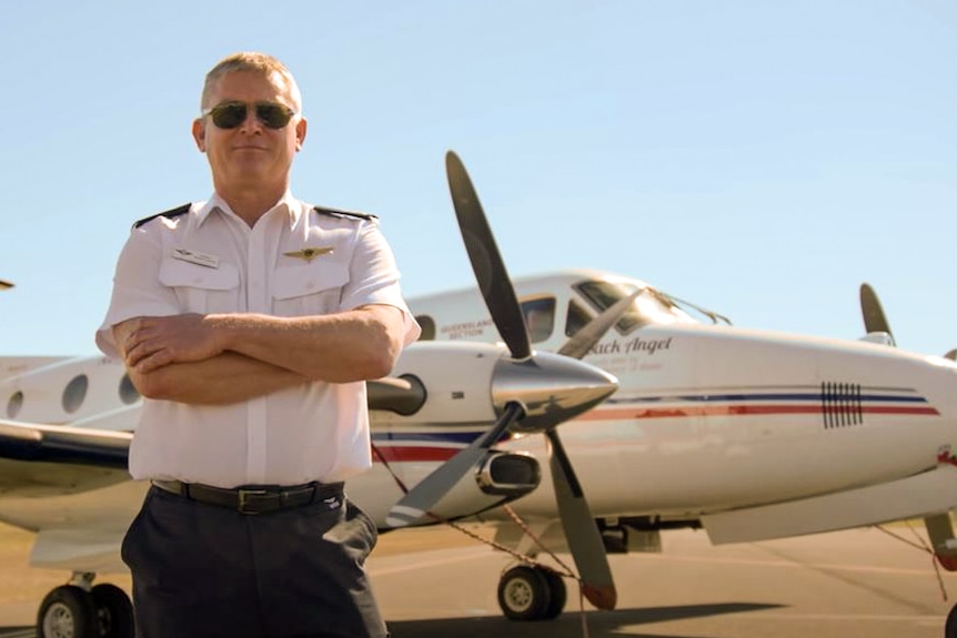 A pilot stands, arms crossed, in front of a small RFDS plane.