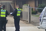 Two uniformed police officers speak to a masked detective outside a suburban house.