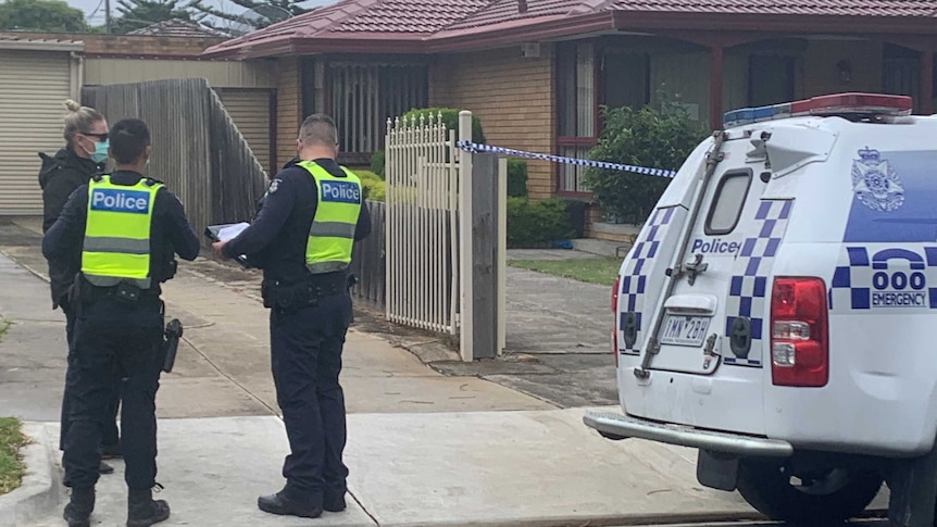 Two uniformed police officers speak to a masked detective outside a suburban house.