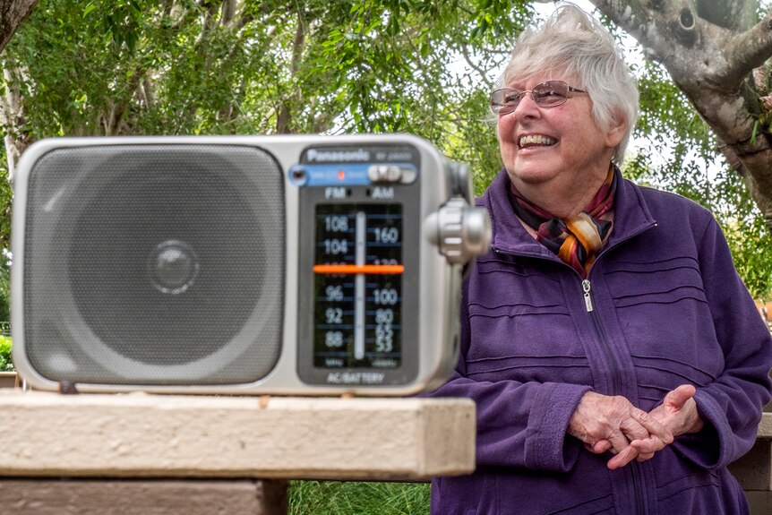 A woman stands behind a battery radio.