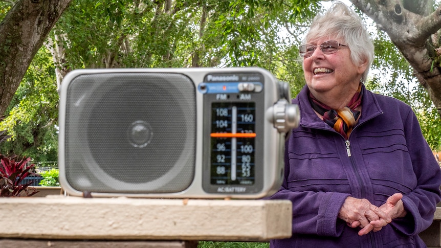 A woman stands behind a battery radio.