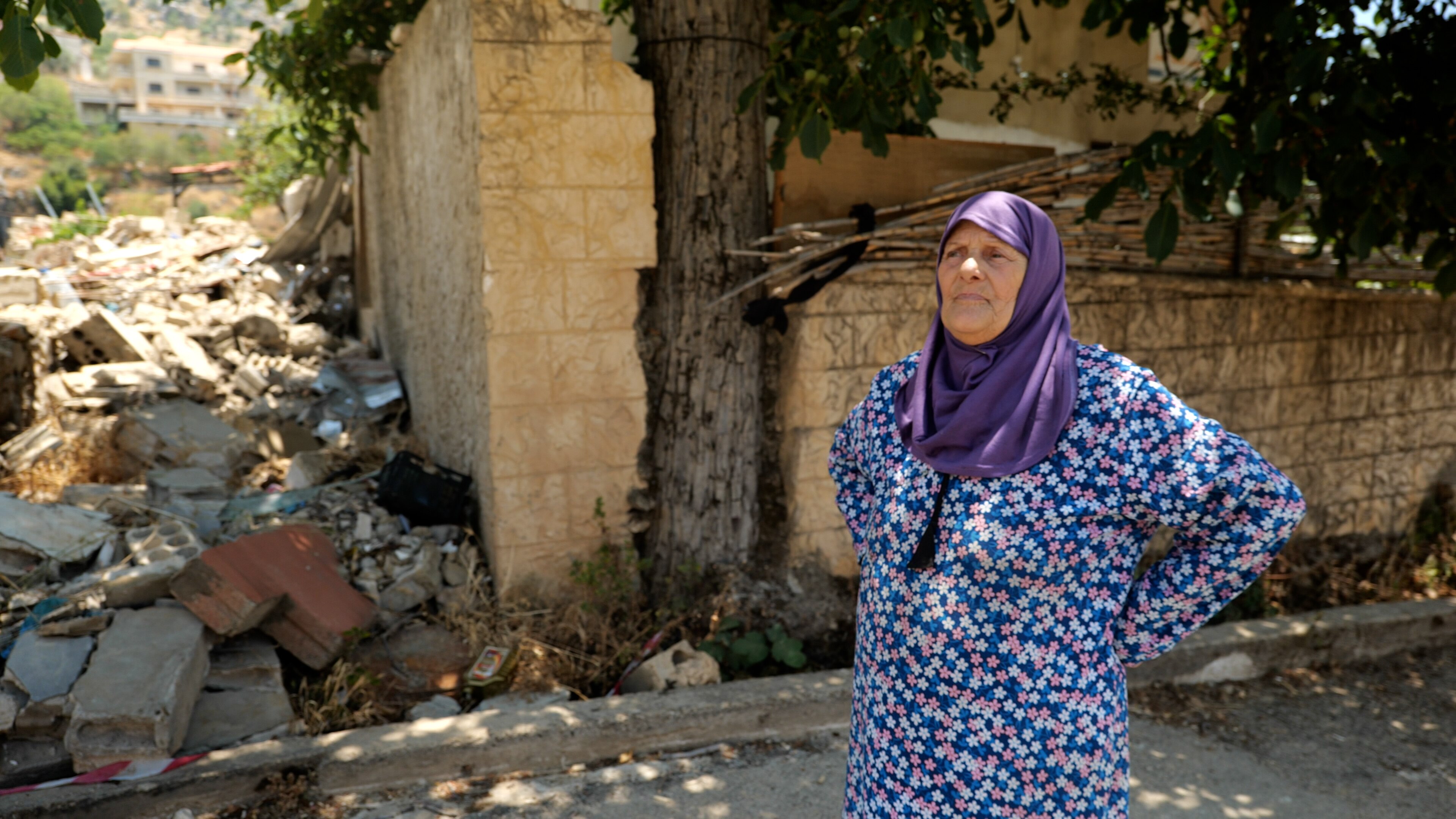 A woman stands in a village dressed in colourful clothing 