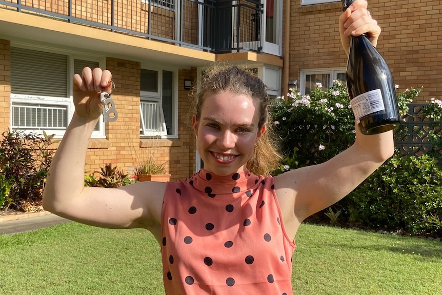 Lizzie holds up house key sand a bottle of champagne.