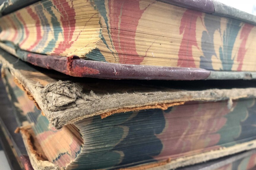 Thick old books with fraying hard covers and patterned printing on the page edges.