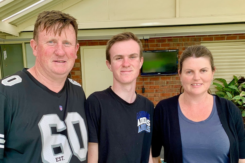 Kellie, Brendan and their son Zane stand smiling in front of their brick home with a garage.