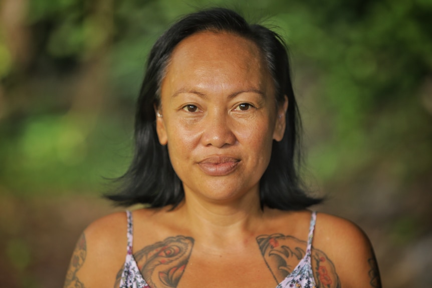 A woman with black hair has tattoos on her chest and arm.