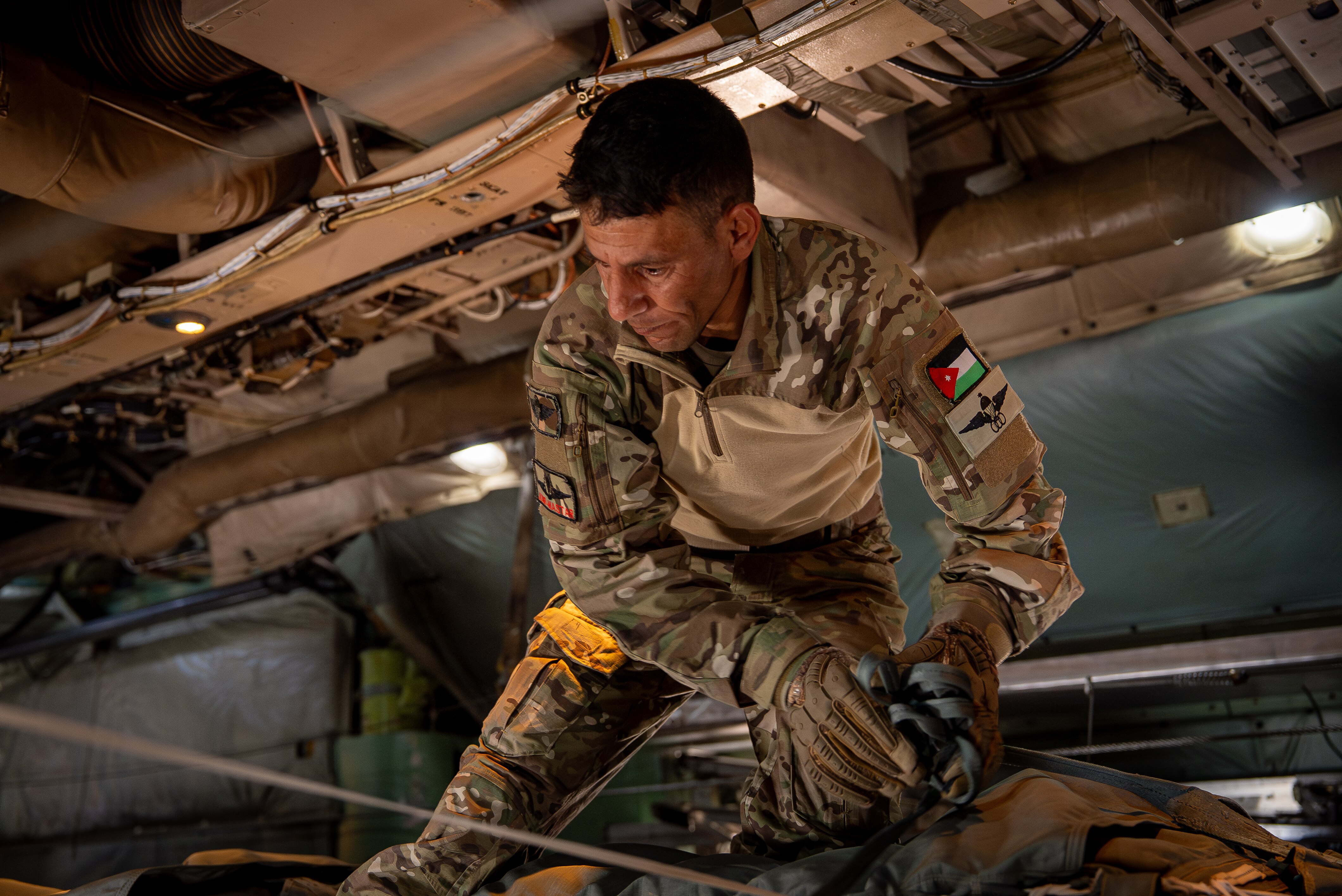 A soldier fixes a pallet of aid to an air drop mechanism inside a military cargo plane.