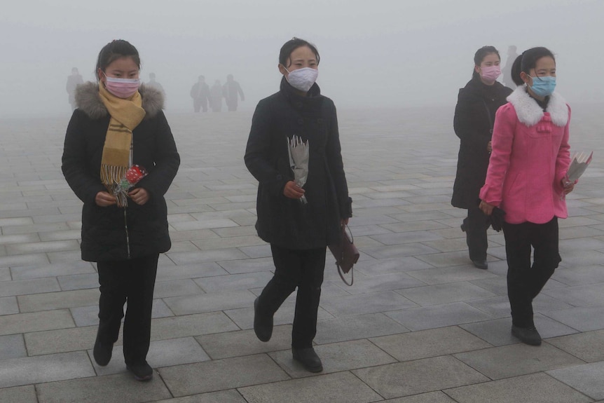 Four women wearing face masks walk through a foggy square