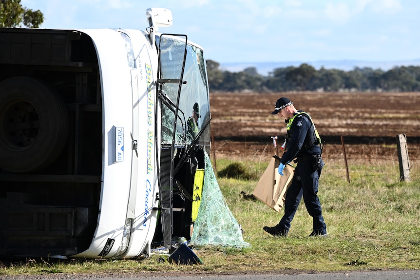 Bus turned upside down with a police officer removing a loose item.