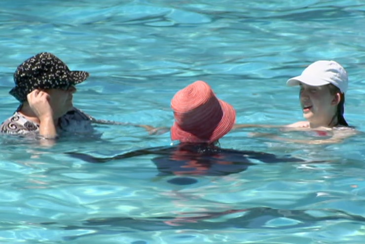 Three women wearing hats cool down in a public swimming pool.