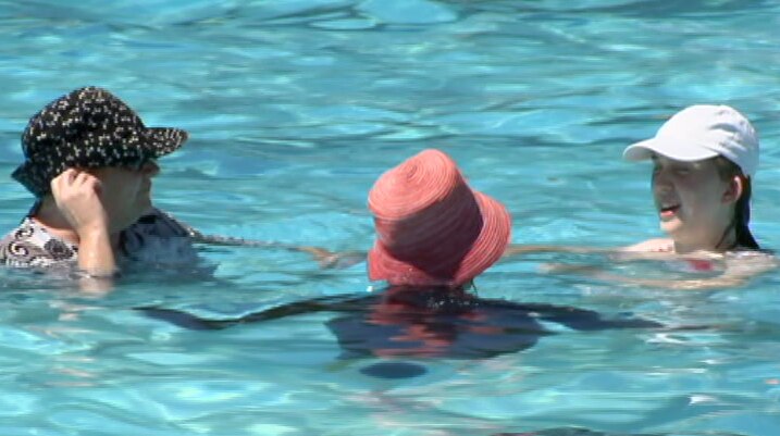 Three women wearing hats cool down in a public swimming pool.