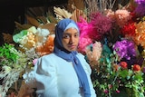 A woman wearing the hijab standing in front of a floral background.