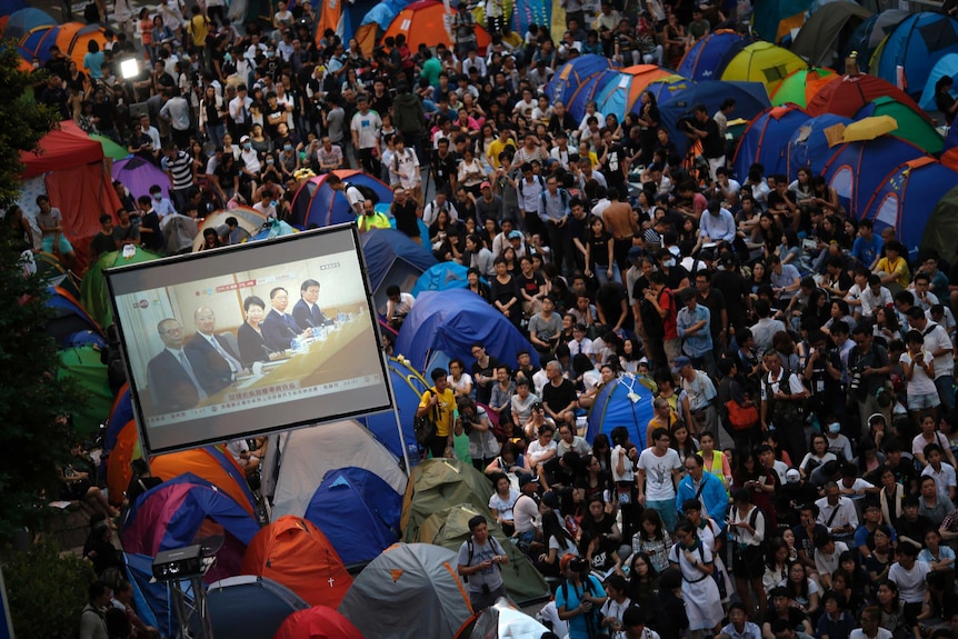 Hundreds of people watch a screen with politicians in the streets of Hong Kong.