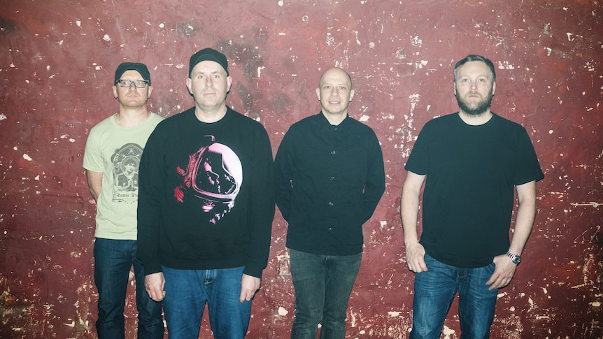 Scottish band Mogwai stand against a red-flecked wall for a press photo