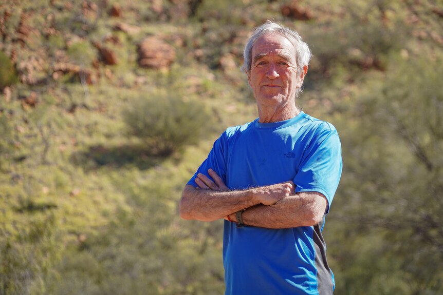 fit man aged in his 70s wearing a blue shirt with red desert bushland behind him