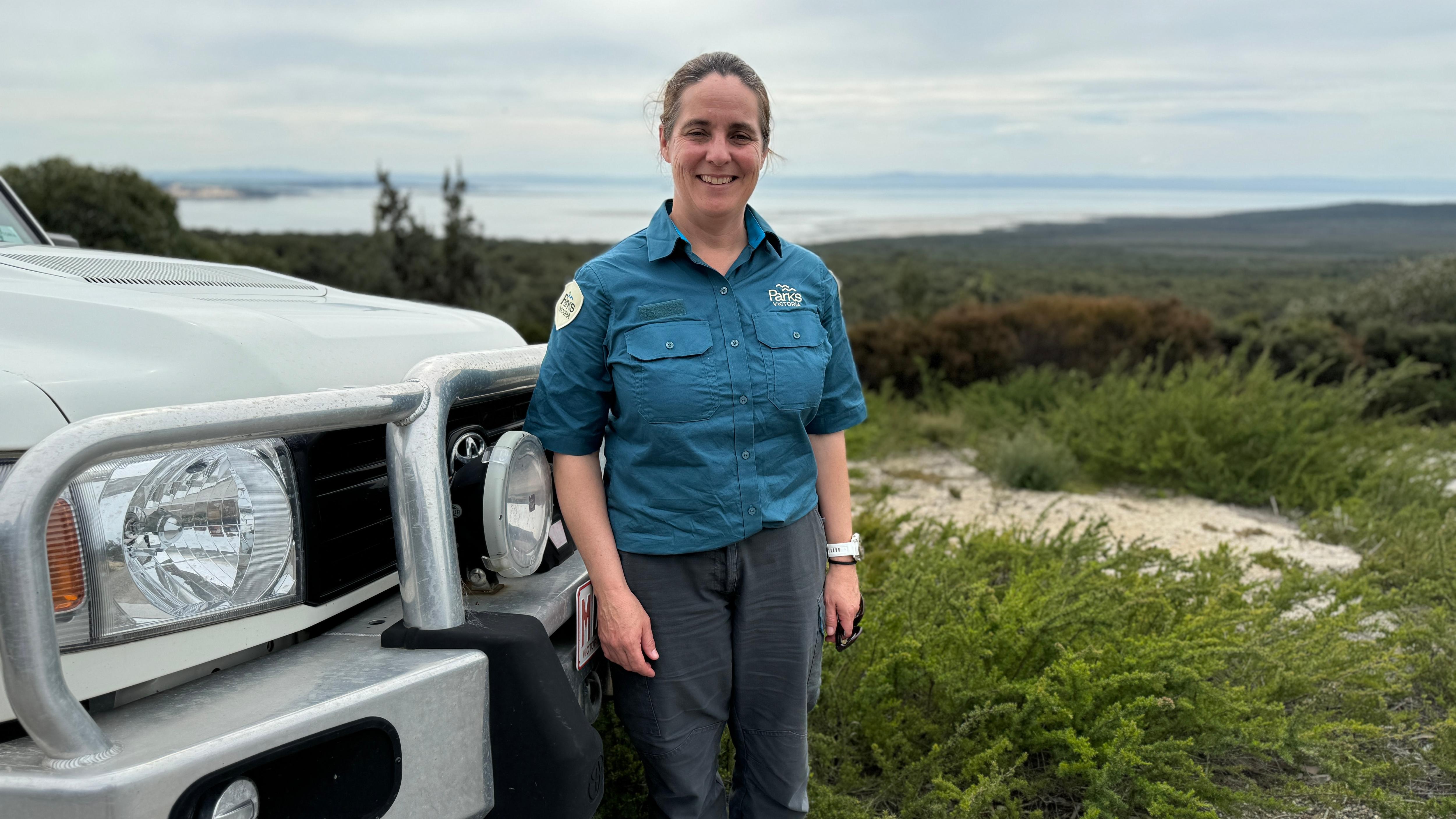 Emily Green stands in front of her Parks Victoria vehicle, Wilsons Promontory is in the background