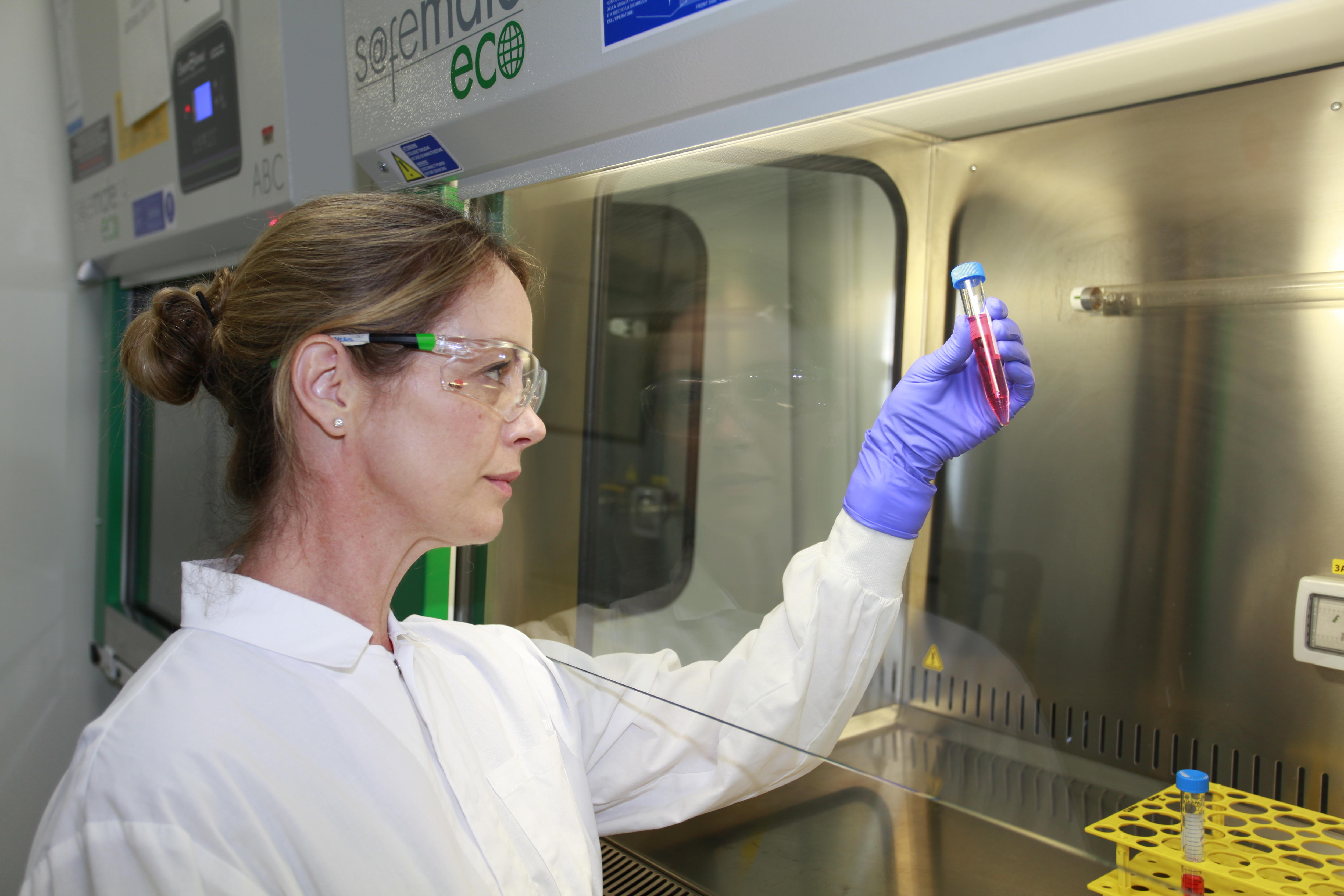 A woman in a lab coat holds up a test tube with red