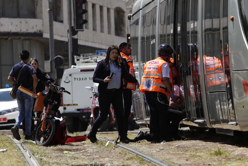 five emergency workers wearing hi vis attend to the scene on the light rail tracks in jerusalem