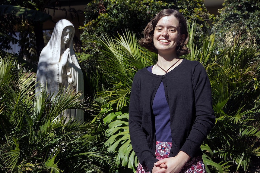 A woman stands in a garden in front of a statue of Mary