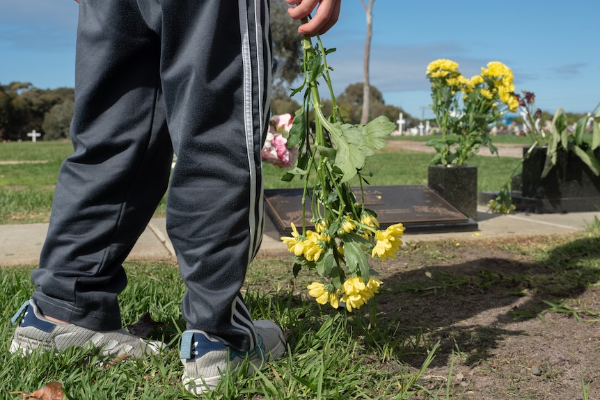 Child holding a bouquet of flowers in front of grave