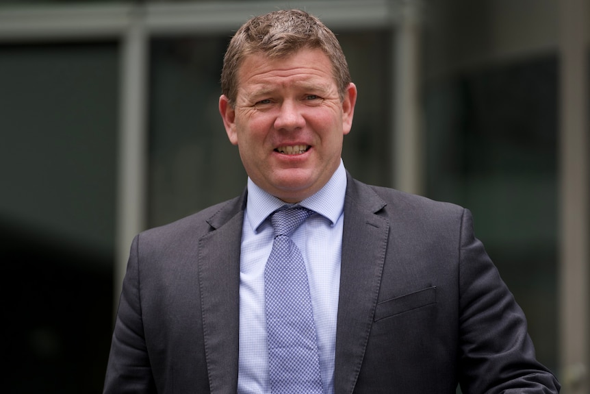 A mid shot of a grimacing Michael Tudori outside court wearing a suit and tie.