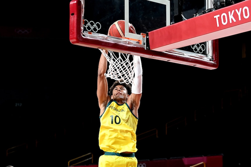 An Australian male basketballer scores a basket with a slam dunk at the Tokyo Olympics.