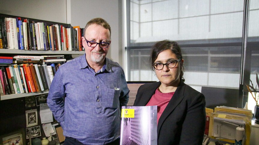 Dr Vicki Senta holds her report at UNSW, she is wearing glasses and is standing next to a tall white man, another researcher.