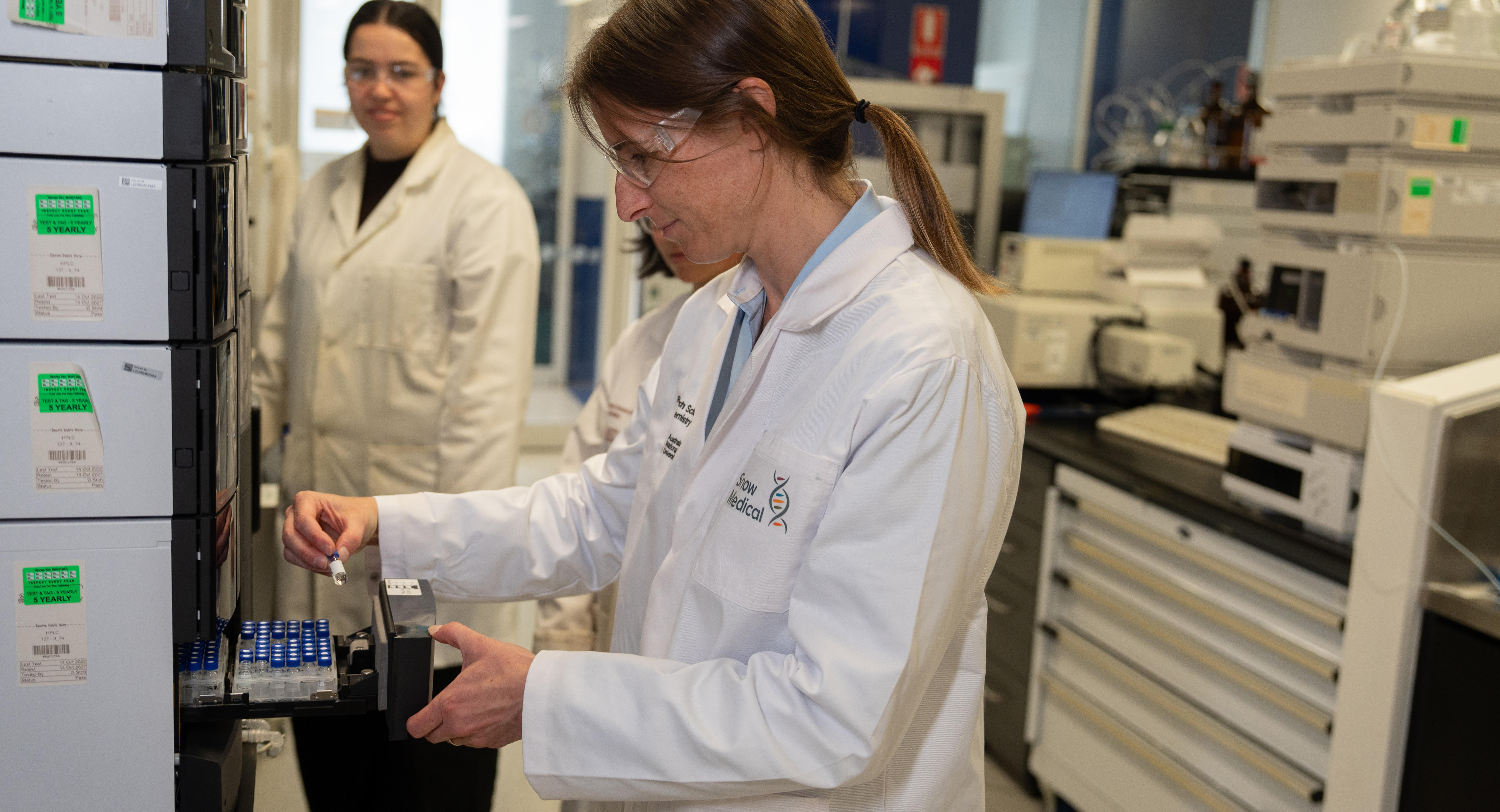 Uma mulher vestindo um jaleco olha para um pequeno tubo transparente em um laboratório. 