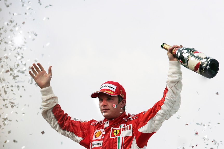Kimi Raikkonen holds a bottle of champagne in one hand with both hands raised