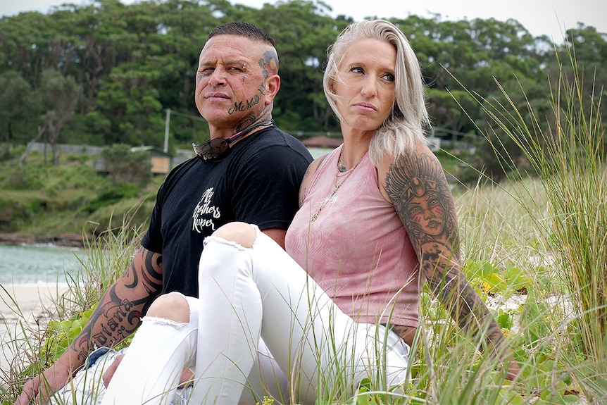 James and Kulani Williams sit on a sand dune with water and Wreck Bay village in the background.