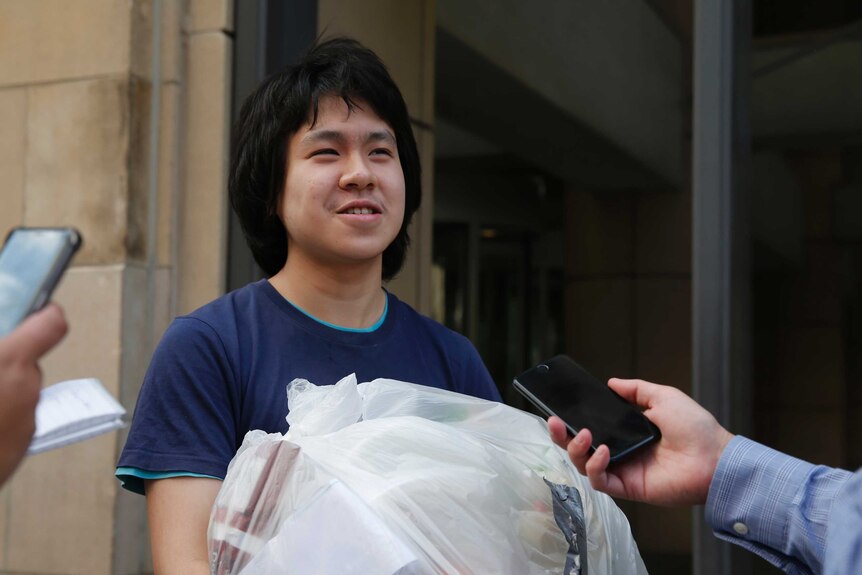 Amos Yee, carrying a plastic bag full of his belongings, talks to reporters.