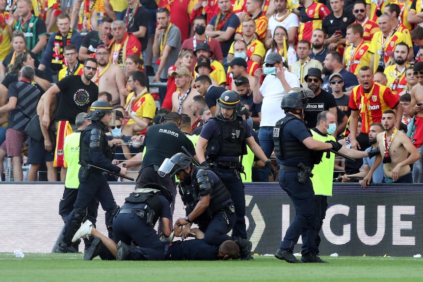 Un homme est retenu par la police en tenue anti-émeute alors qu'une foule de supporters regarde