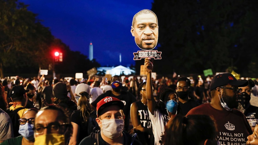 A crowd of people packed together on a street, the Washington Monument just visible in the background