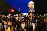 A crowd of people packed together on a street, the Washington Monument just visible in the background