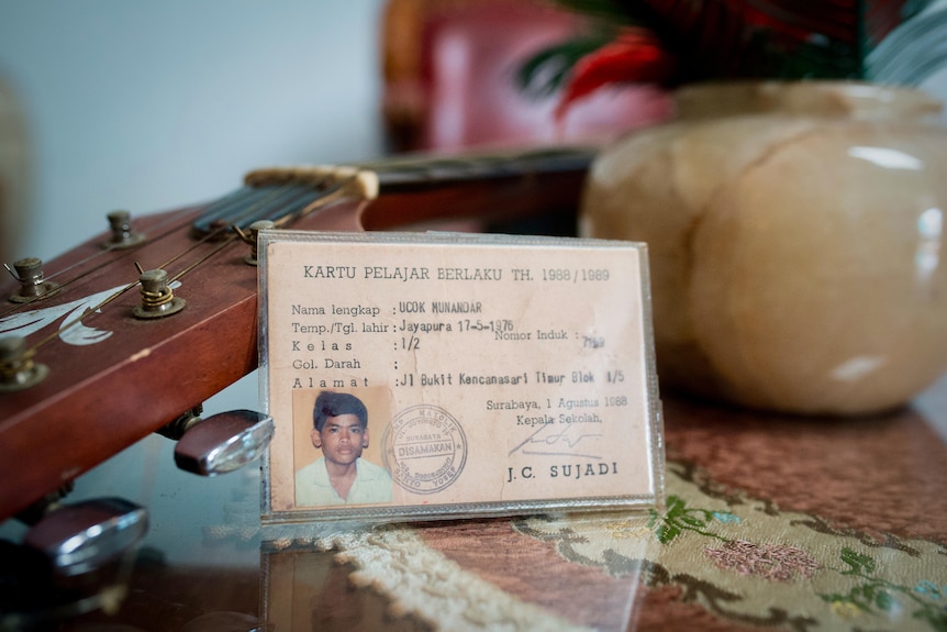 A close-up shows an ID card leaning against the neck of a guitar