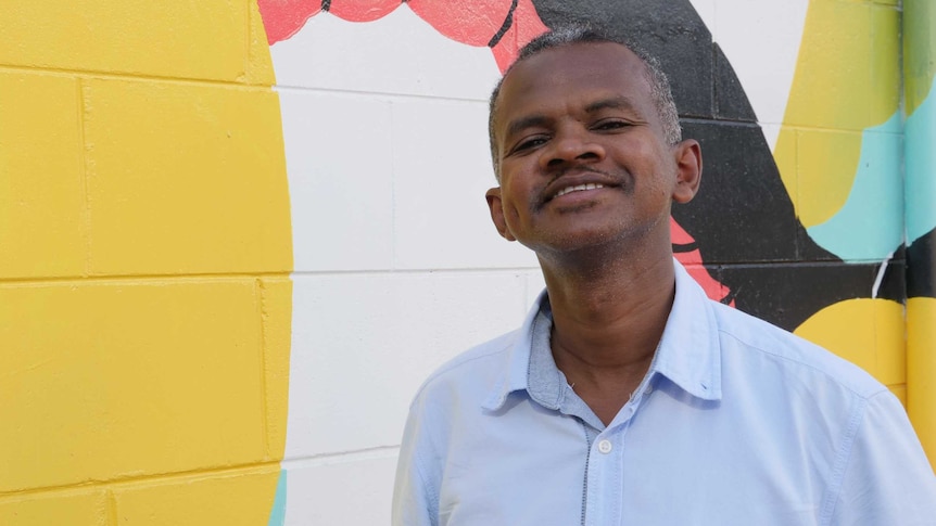 African male smiling at the camera with colourful wall in the background.