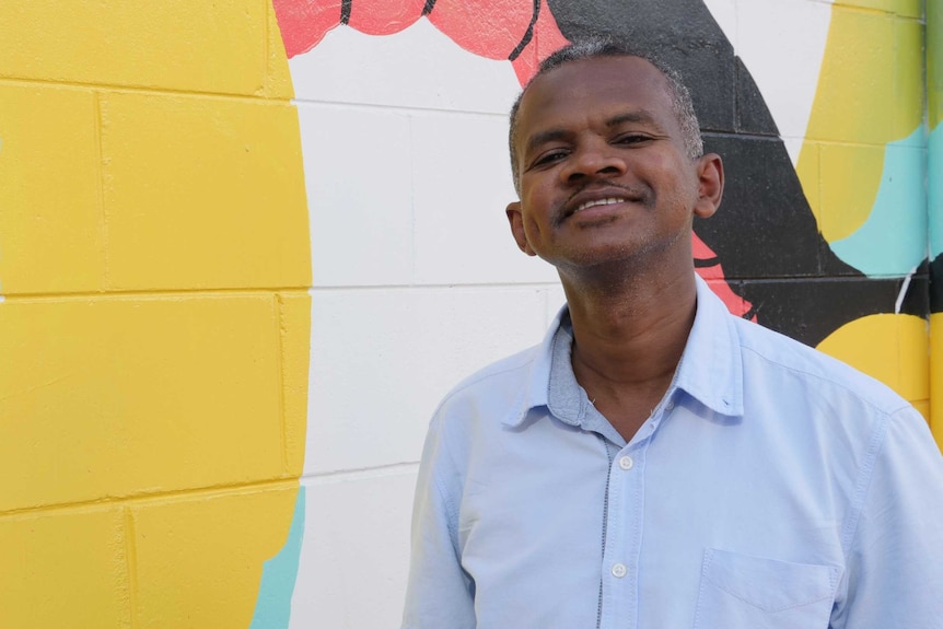 African male smiling at the camera with colourful wall in the background.